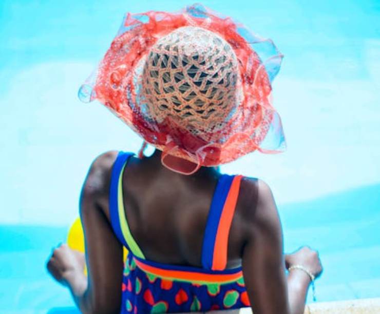 Donna che prende il sole, con cappello, a bordo piscina